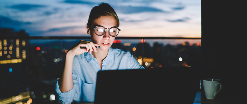 A woman trader wearing glasses sits at a table with a laptop, focused on psychology and emotions in forex trading.