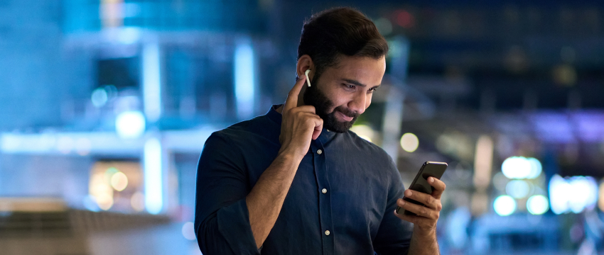 A trader man with a beard wearing a blue shirt is engaged in a phone conversation, possibly about mobile forex algo trading.