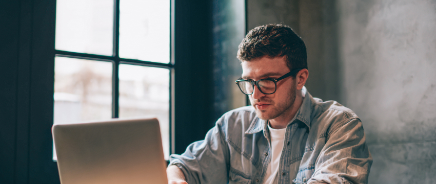 A man in glasses using his laptop for forex trading, showcasing a successful trading environment.