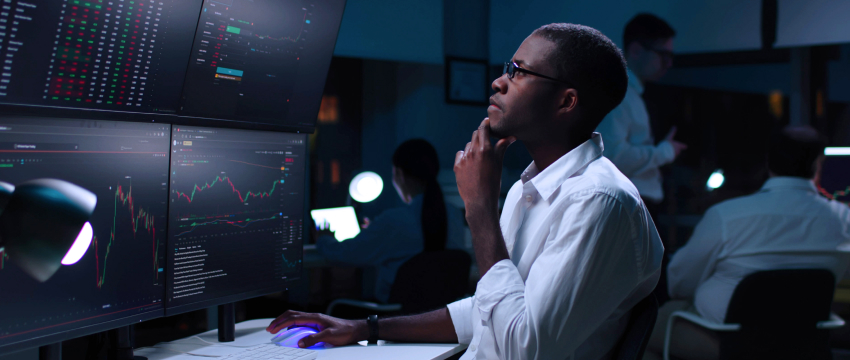 Um homem sentado à escrivaninha com vários monitores, revisando estratégias de trading de forex para evitar erros comuns e alcançar o sucesso.