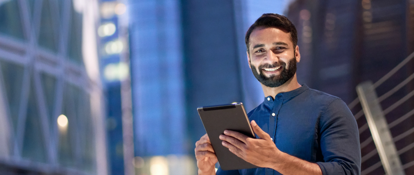 A man with a beard wearing a blue shirt is engaged with a tablet, symbolizing a novice in forex trading.