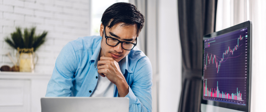 A man trader in glasses studies a stock chart displayed on his computer, engaged in trading analysis using MetaTrader 4.